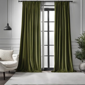 May include: A pair of dark green velvet curtains hanging in a living room with a white rug, a white chair, and a potted plant.