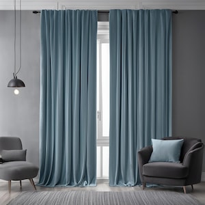 May include: A pair of light blue curtains hanging in a living room with a gray armchair and a small table lamp.