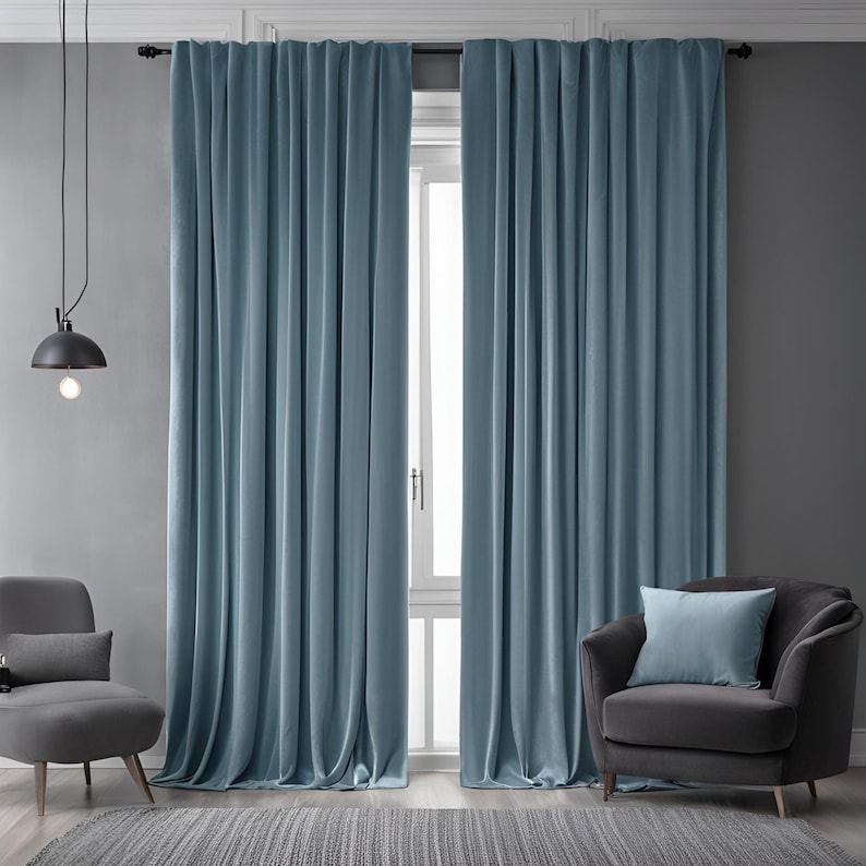 May include: A pair of light blue curtains hanging in a living room with a gray armchair and a small table lamp.