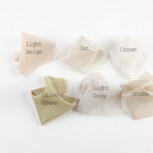 May include: Six fabric swatches with frayed edges arranged in a group. The colors are labeled as Light Beige, Oat, Cream, Olive Green, Light Gray, and Stone. Each piece of fabric has a soft, textured appearance and is displayed against a plain white background.