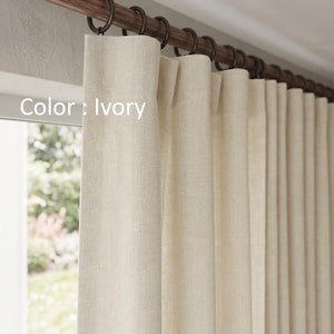 May include: Ivory curtains with a textured fabric finish hanging from a dark brown wooden rod with matching circular rings. The text Color : Ivory is visible on the left side of the curtain panel, which features a pleated header design.