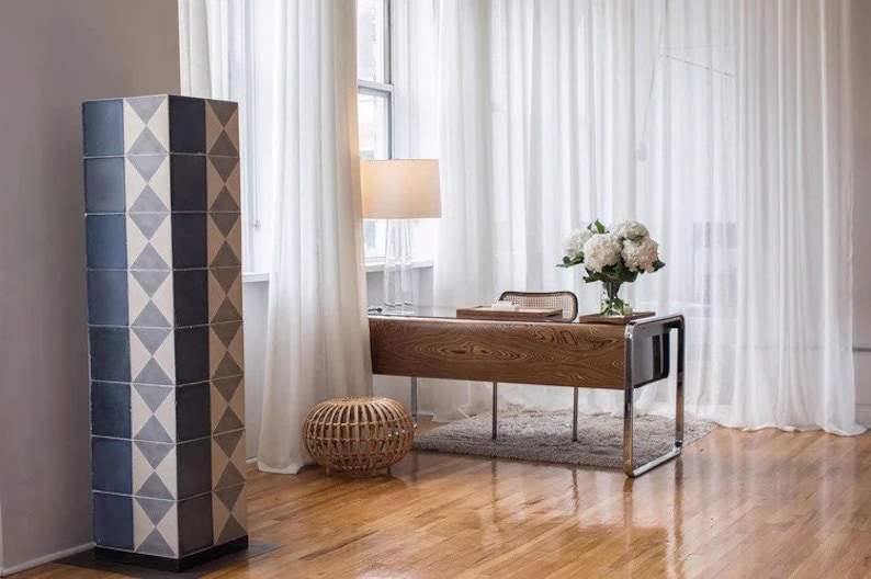 May include: A tall, rectangular floor lamp featuring a geometric pattern of dark blue and off-white diamond tiles. The structure is vertical and slender, standing on a flat base, with a repeating grid design that covers all visible sides of the column.