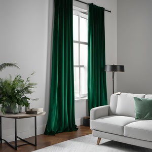 K&ouml;nnte beinhalten: Zwei smaragdgr&uuml;ne Samtvorh&auml;nge h&auml;ngen in einem Wohnzimmer mit einem wei&szlig;en Sofa und einer Stehlampe. Die Vorh&auml;nge sind vollst&auml;ndig zugezogen und blockieren das Licht vom Fenster.