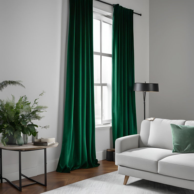 K&ouml;nnte beinhalten: Zwei smaragdgr&uuml;ne Samtvorh&auml;nge h&auml;ngen in einem Wohnzimmer mit einem wei&szlig;en Sofa und einer Stehlampe. Die Vorh&auml;nge sind vollst&auml;ndig zugezogen und blockieren das Licht vom Fenster.