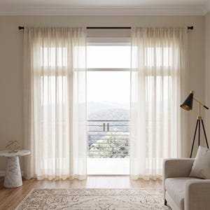 May include: A pair of floor-length, sheer off-white curtains hanging from a dark rod over a large window. The curtains feature a subtle vertical striped texture, allowing soft light to filter through while maintaining a light and airy appearance.