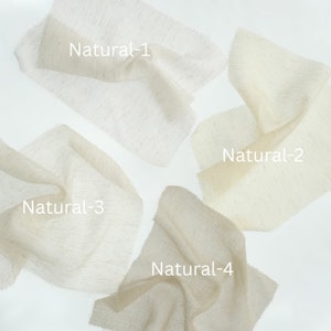 May include: Four swatches of off-white, textured fabric arranged on a plain background. Each piece of fabric is labeled with white text: Natural-1, Natural-2, Natural-3, and Natural-4. The material has a visible weave and slight variations in color.