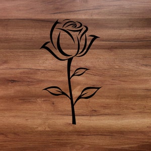 May include: A black silhouette of a rose with a stem and leaves on a brown wood background.