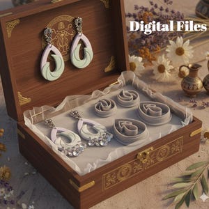 May include: A wooden jewellery box displays two pairs of earrings and several grey clay cutters. The earrings feature a teardrop design with pastel green and lavender accents. The box has gold-coloured hardware and the text "Digital Files".