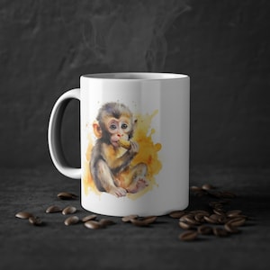 May include: White ceramic coffee mug featuring a watercolour illustration of a baby monkey eating a peanut. The monkey is sitting on a yellow watercolour background.
