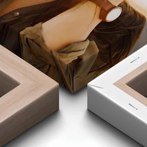 Close-up of two canvas frames showing the corner folds and a light wood grain frame next to a white frame, with a person in an olive green shirt visible in the background.