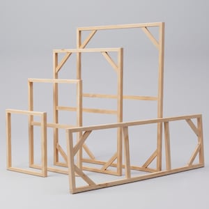 A cluster of empty rectangular wooden stretcher bars in various sizes standing on a light gray surface.