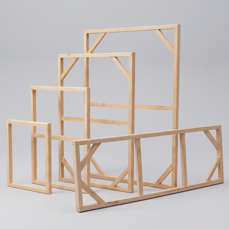 A cluster of empty rectangular wooden stretcher bars in various sizes standing on a light gray surface.