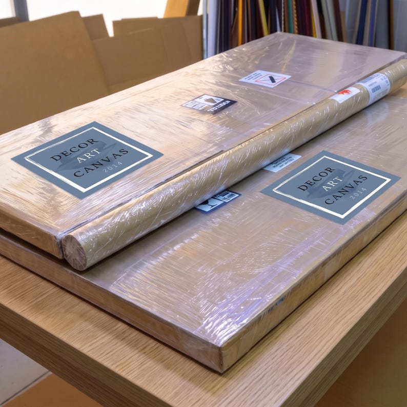 Two packaged flat canvases and one rolled canvas wrapped in clear plastic on a wooden workbench with Decor Art Canvas stickers visible.
