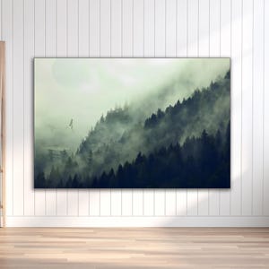 A horizontal framed canvas hanging on a white paneled wall depicting a misty pine forest landscape with a flying spacecraft.