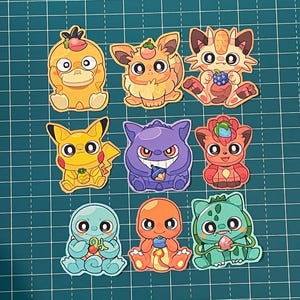 May include: Nine colorful cartoon character stickers. The stickers feature various creatures in shades of yellow, orange, purple, red, blue, and green. Each sticker has a unique design and expression, with some holding objects.