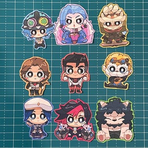 May include: A collection of colorful cartoon character stickers. Each sticker features a different character with large eyes and unique outfits. The stickers are arranged on a green grid background.