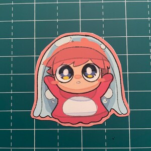 以下が含まれることがあります： 赤い髪と赤い衣装の漫画のキャラクターが、青い半透明の泡で覆われたステッカー。キャラクターは大きな目を持ち、驚いた表情をしています。ステッカーは緑色のグリッド上にあります。