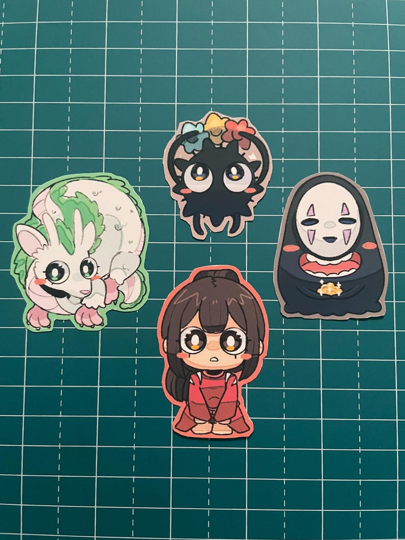 以下が含まれることがあります： アニメスタイルのカラフルなステッカー5枚のコレクション。緑色のアクセントが付いた白い生き物、花の冠をつけた黒い生き物、赤い衣装のキャラクターなど、さまざまなデザインのキャラクターが描かれています。