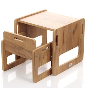 May include: A wooden children's table and chair set. The table has a rectangular top and is supported by four sides with cut-out handles. The chair has a backrest with a handle and a seat. The set is made of light brown wood with a wood grain pattern.