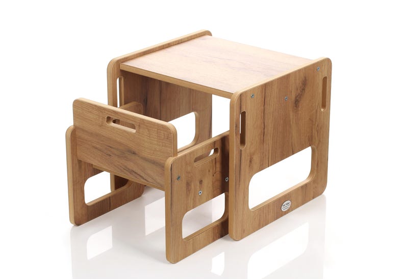 May include: A wooden children's table and chair set. The table has a rectangular top and is supported by four sides with cut-out handles. The chair has a backrest with a handle and a seat. The set is made of light brown wood with a wood grain pattern.
