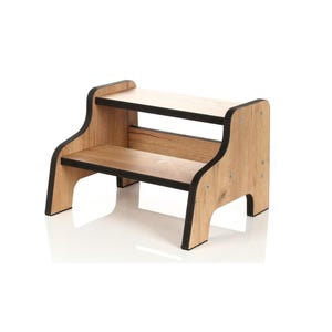 May include: A two-step stool constructed from light brown wood-grain panels with contrasting black edges. The design features two horizontal platforms supported by side panels secured with visible silver-toned metal screws on the exterior.