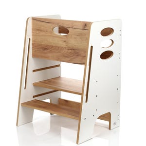 Può includere: Uno sgabello a gradini bianco e effetto legno a tre livelli. La sezione superiore presenta un pannello effetto legno con un'apertura per la maniglia. I lati sono bianchi con fori ovali e i livelli inferiori sono ripiani in legno. Per bambini.