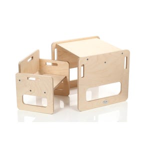 Può includere: Un set di tavolo e sedia per bambini in legno chiaro. Il tavolo è un piccolo cubo con un piano piatto. La sedia è anch'essa a forma di cubo con seduta e schienale. Entrambi hanno maniglie ritagliate.