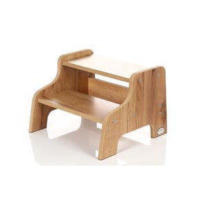 Puede incluir: Un taburete de madera de dos peldaños con un acabado natural. El taburete tiene un peldaño superior y un peldaño inferior, ambos hechos de madera. El taburete es robusto y bien hecho, y sería perfecto para ayudar a los niños a alcanzar superficies más altas.