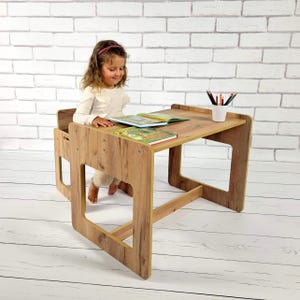 Könnte beinhalten: Ein hölzernes Kinder-Schreibtisch- und Stuhl-Set mit natürlicher Holzmaserung. Der Schreibtisch hat eine rechteckige Oberseite mit erhöhtem Rand und einen integrierten Stuhl. Zwei Bücher liegen auf dem Schreibtisch.