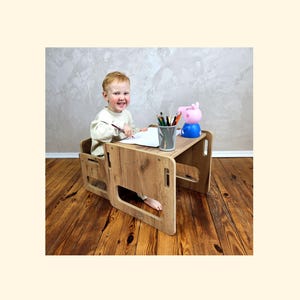 Può includere: Un set di scrivania e sedia per bambini in legno con finitura a venature naturali. La scrivania ha un piano rettangolare e una sedia integrata. Un bambino è seduto alla scrivania, che disegna con pastelli. Un giocattolo di Peppa Pig e un bicchiere di matite sono sulla scrivania.