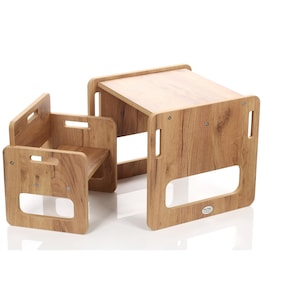 Op de afbeelding: Een kleine houten tafel en stoel set met een lichtbruine houtnerf afwerking. De tafel heeft een rechthoekig blad en de stoel heeft een zitting en rugleuning. Beide hebben uitgesneden handgrepen.