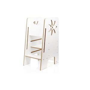 May include: A white wooden learning tower with two steps and a cutout flower design on the side panel. The structure features a tall frame with a handle opening at the top and exposed light-coloured wood edges along the vertical support panels.