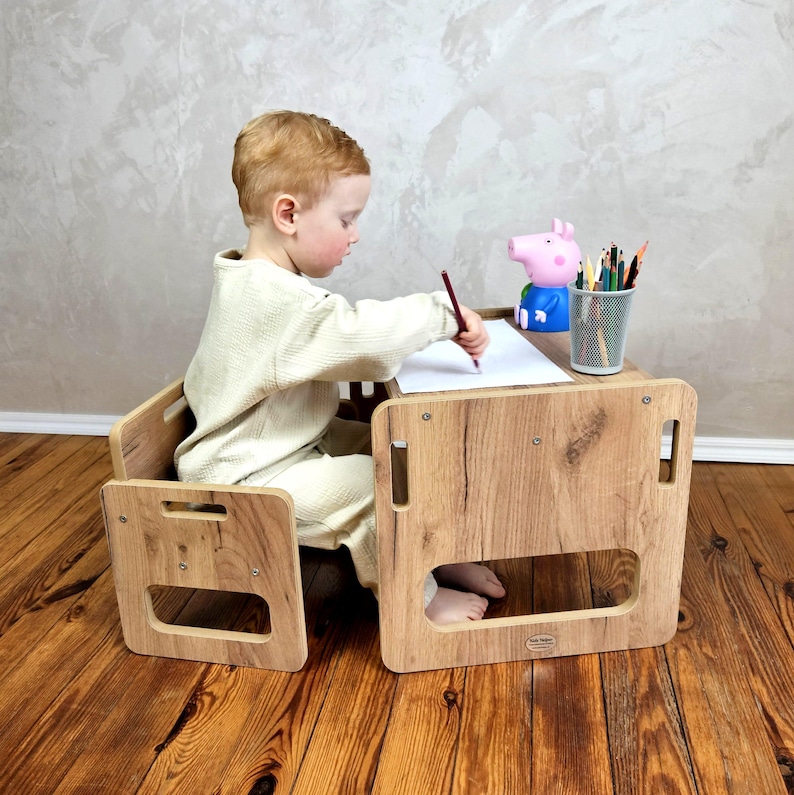 May include: A wooden children's desk and chair set with a light wood grain finish. The desk has a rectangular top with a small opening for the legs. A child is seated at the desk, drawing with a pencil. A Peppa Pig toy and a pencil holder are on the desk.