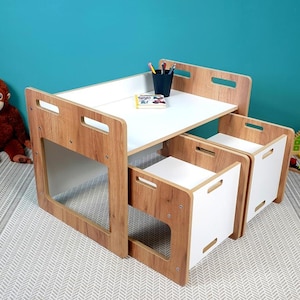Op de afbeelding: Een kinderset met een tafel en twee stoelen van wit en hout. De tafel heeft een wit blad en houten zijkanten. De stoelen zijn wit met houten zijkanten. De set staat op een wit en grijs gestreept tapijt.