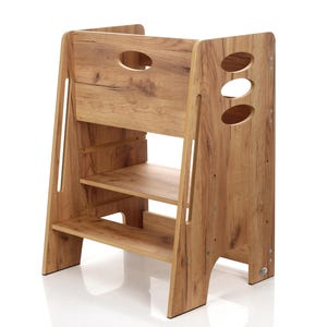 Può includere: Sgabello in legno con finitura a venature naturali. Presenta due ripiani e un ritaglio ovale nella parte superiore. I lati hanno un design a scala. Design robusto e funzionale.