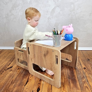 May include: A wooden children's desk and chair set with a light wood grain finish. A young child is seated at the desk, drawing with colored pencils. A pink and blue Peppa Pig figurine sits on the desk. The desk is on a wooden floor.