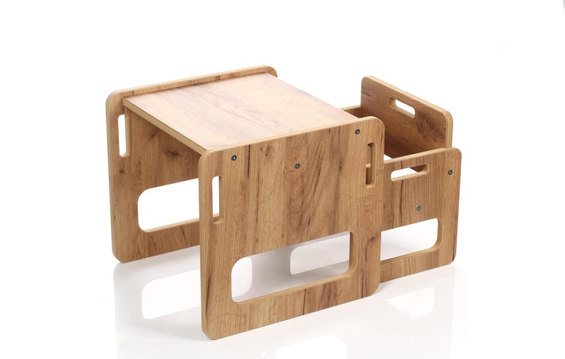 May include: A wooden children's table and chair set. The table has a rectangular top and is supported by four legs with cut-out handles. The chair has a similar design, with a backrest and a seat. The set is made of light brown wood.