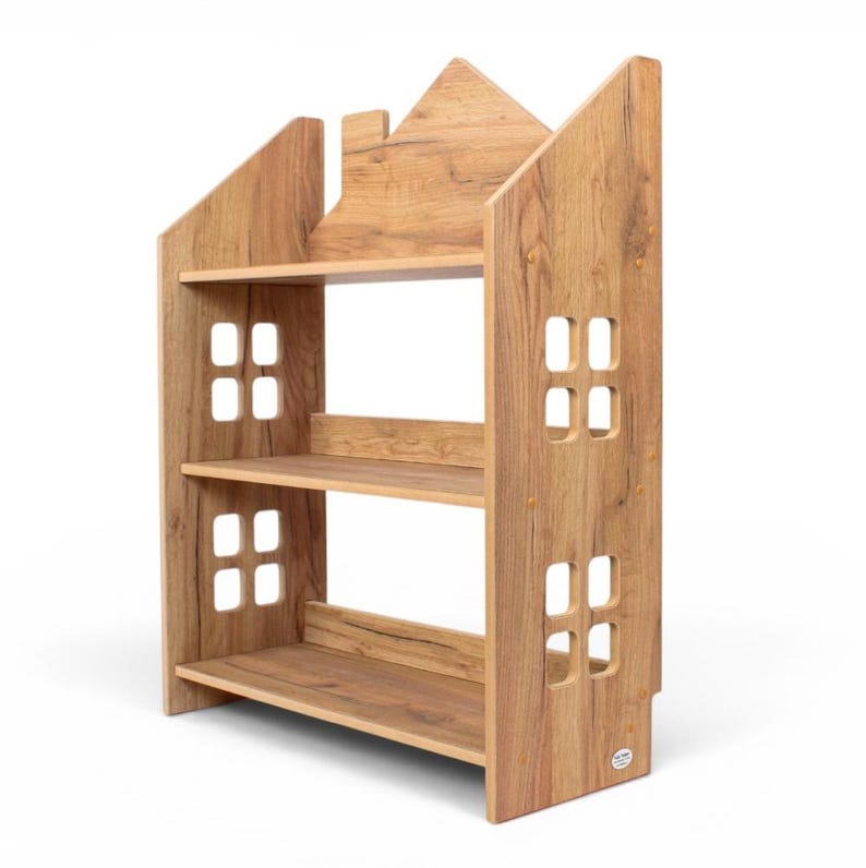 May include: A light brown wooden bookshelf shaped like a house with three horizontal shelves. The side panels feature cut-out square window designs. The top of the unit has a peaked roof silhouette, and the wood grain is visible throughout the structure.