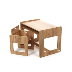 Könnte beinhalten: Ein hellbraunes Kindertisch- und Stuhlset aus Holz. Der Tisch hat eine rechteckige Oberseite und ein unteres Regal. Die Stühle haben quadratische Rückenlehnen mit einem Griffausschnitt. Das Set besteht aus Holz mit Holzmaserung.