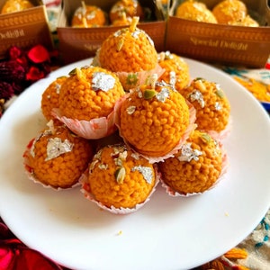 Peut inclure: Gros plan sur une assiette de petites douceurs rondes de couleur orange. Les douceurs sont recouvertes de petites pépites blanches et ont un dessus en feuille d'argent. Les douceurs sont disposées en tas sur l'assiette.
