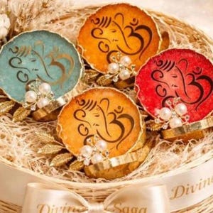 Può includere: Un cestino intrecciato pieno di sottobicchieri decorativi. I sottobicchieri sono rotondi con un bordo dorato e presentano un simbolo religioso in vari colori: verde acqua, arancione e rosso. Ogni sottobicchiere è adornato con perle e dettagli dorati.