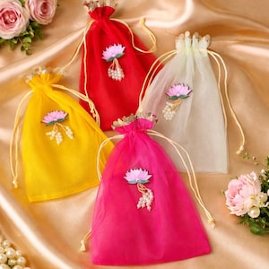 Op de afbeelding: Vier kleurrijke trekkoordzakjes in rood, geel, roze en wit. Elk zakje is versierd met een lotusbloem en parelaccenten. De zakjes hebben gouden randen en beige trekkoorden, perfect voor kleine cadeautjes.