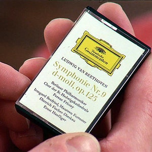 May include: A cassette tape held in hand, featuring a Deutsche Grammophon label. The label displays the title "Symphonie Nr. 9 d-moll, op. 125" by Ludwig van Beethoven, with text detailing the performers.