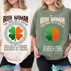 以下が含まれることがあります： 「IRISH WOMAN THE SOUL OF A WITCH」の文字が入った、アイボリーとモスグリーンの2枚のTシャツ。中央には緑とオレンジのシャムロック。テキスト「THE FIRE OF A LIONESS THE HEART OF A HIPPIE THE MOUTH OF A SAILOR」が下にあります。