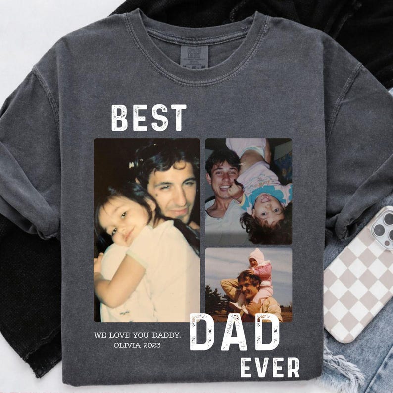 Pode incluir: Camisola cinza escuro com uma colagem de fotos de fam&iacute;lia. As palavras "BEST DAD EVER" est&atilde;o impressas em branco, juntamente com o texto "WE LOVE YOU DADDY. OLIVIA 2023". A camisola tem um aspeto vintage e desgastado.