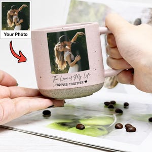May include: A light pink ceramic mug with a speckled texture and a grey base. The mug features a rectangular photo print of a couple embracing, with the printed text "The Love of My Life" and "FOREVER TOGETHER" followed by a small heart icon.