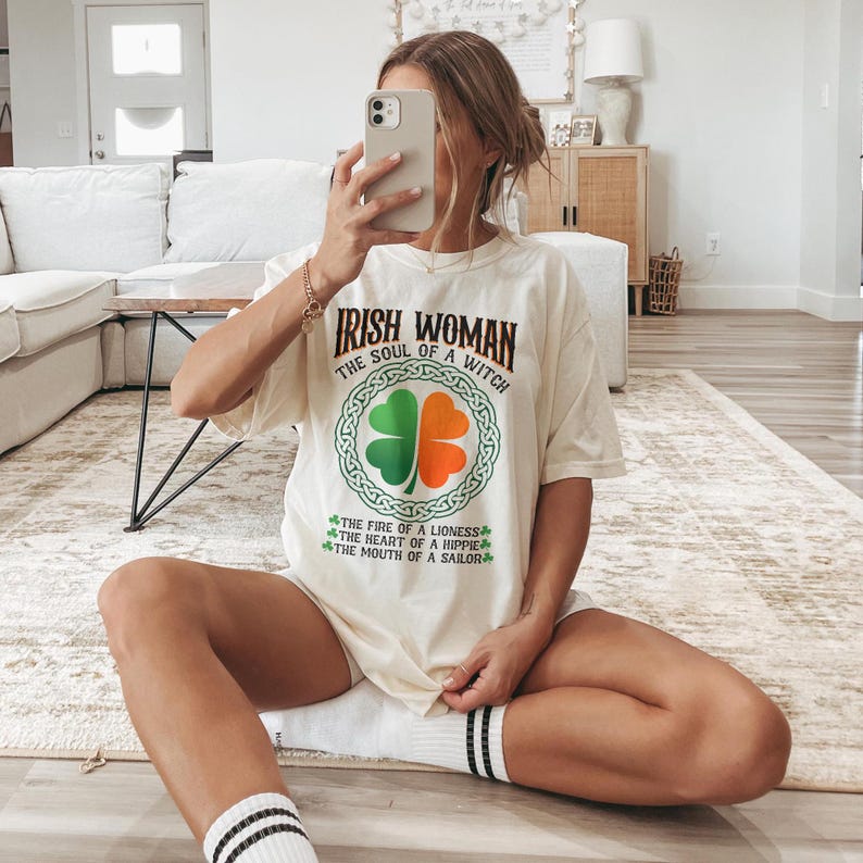 以下が含まれることがあります： 「Irish Woman, The Soul of a Witch」の文字が入ったクリーム色のTシャツ。緑とオレンジのクローバーのデザインが特徴です。「The Fire of a Lioness, The Heart of a Hippie, The Mouth of a Sailor」の文字も含まれています。
