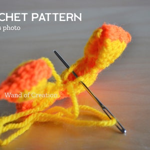 May include: A close-up of a crochet project in progress. The project uses yellow and orange yarn, with two needles inserted. The text "CROCHET PATTERN progress photo" and "Wand of Creation" are visible.