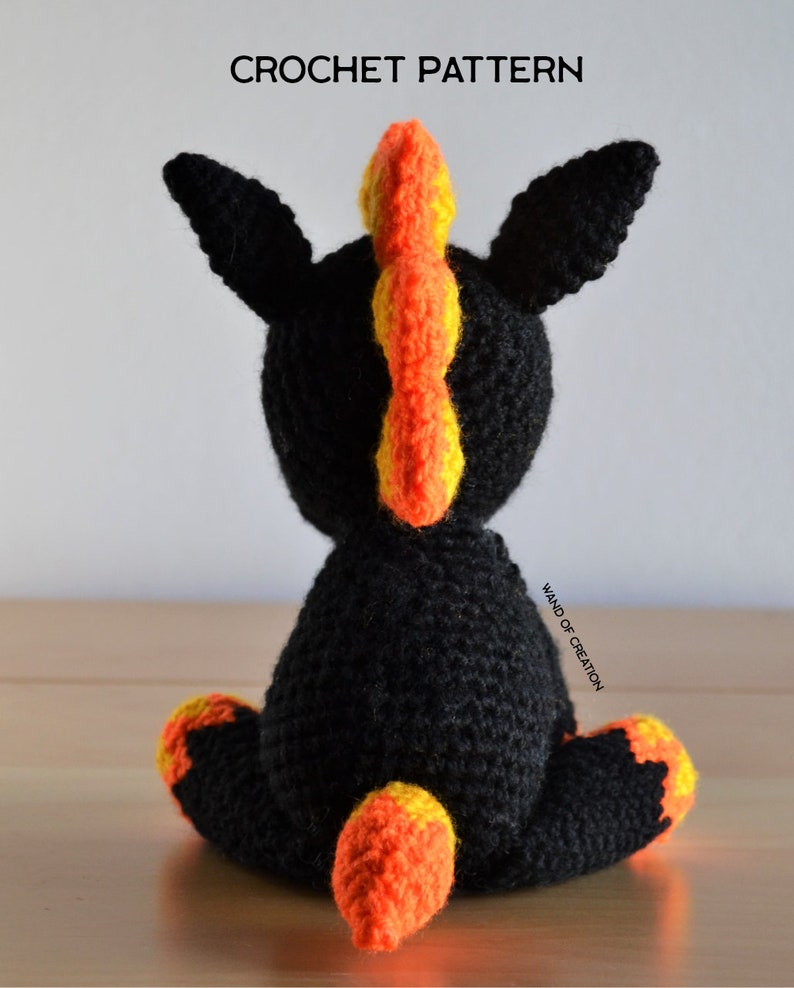 May include: A crocheted unicorn toy in black, featuring orange and yellow details. The mane and tail are in vibrant orange and yellow. The image includes the text "CROCHET PATTERN" at the top.