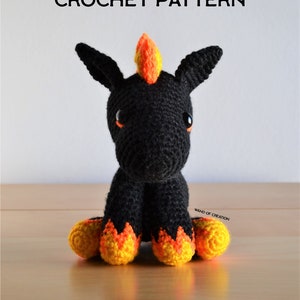 May include: A handcrafted black crochet unicorn with orange and yellow detailing. The unicorn features large, black ears, orange eyes, and a flame-shaped mane. The text "CROCHET PATTERN" is displayed above the unicorn.